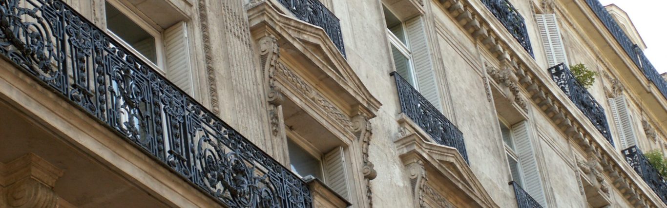 Balcon en fer forgé au-dessus d'une façade en pierre décorée.