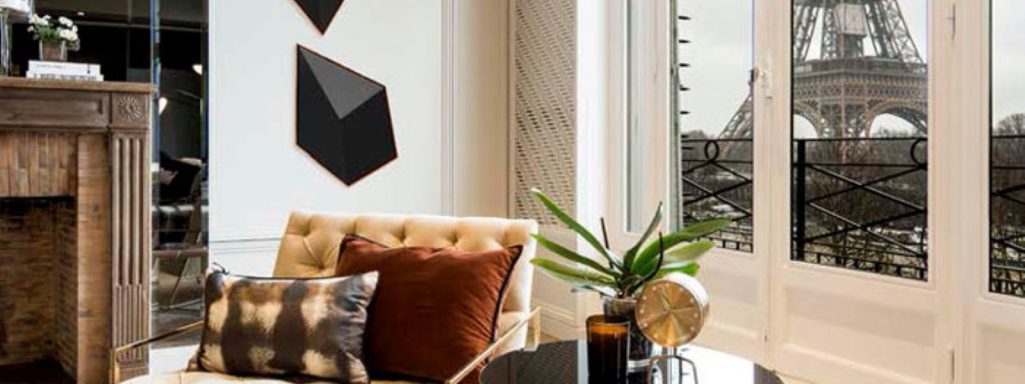 Salon moderne avec canapé, coussins, art mural géométrique et fenêtres ouvertes sur l'extérieur.