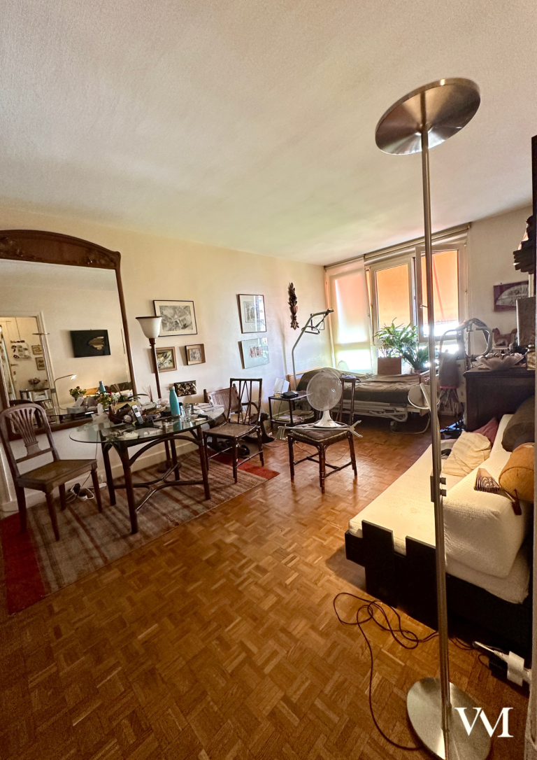 Salon spacieux avec des meubles variés, un lampadaire et des fenêtres éclairant l'espace.