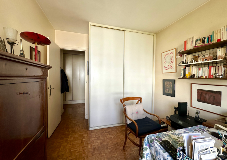 Chambre avec fauteuil, bibliothèque et placard, offrant une ambiance chaleureuse.