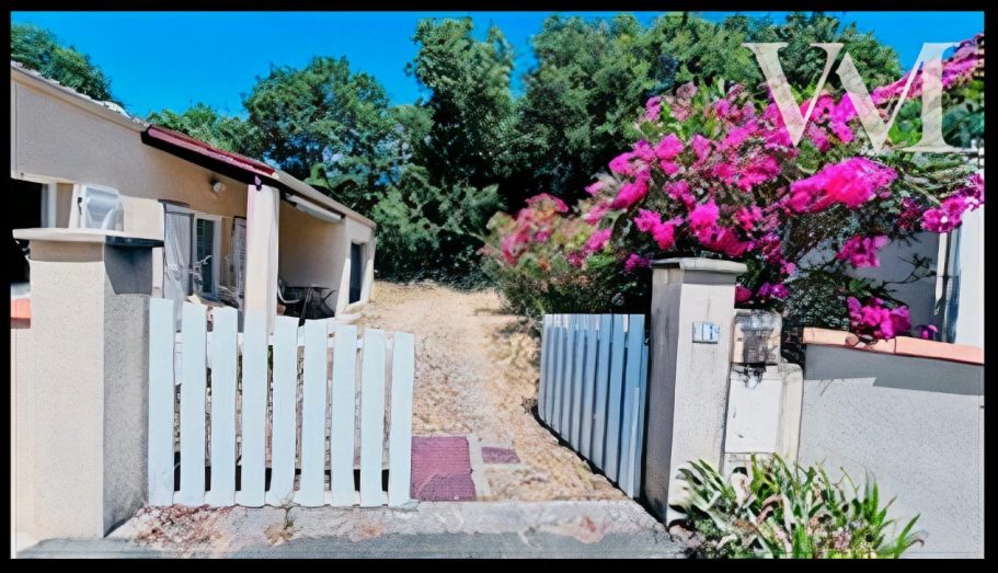 Allée menant à des maisons avec un portail blanc et des bougainvilliers roses.
