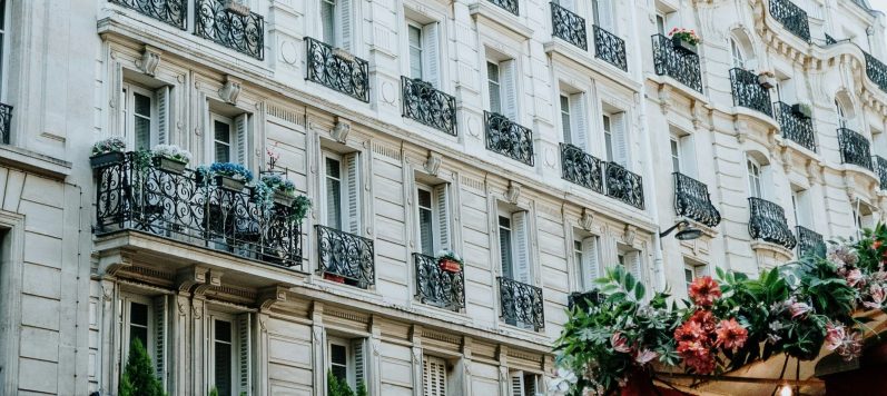 Deux professionnelles du droit au service de votre projet immobilier Façade d'immeuble ancien avec balcons en fer forgé et fleurs colorées.