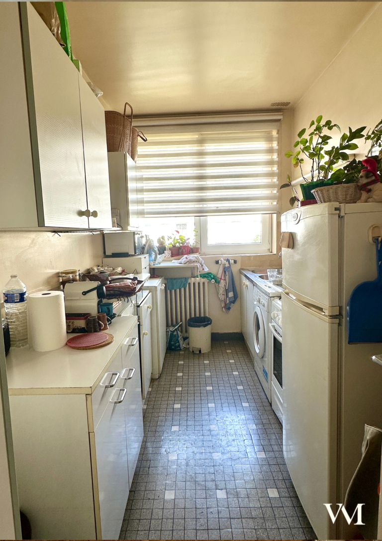 Cuisine étroite avec des armoires blanches, un évier et des appareils ménagers.